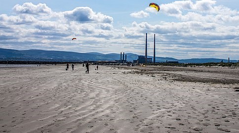 A wide beach surrounded by hills. A kite flies.