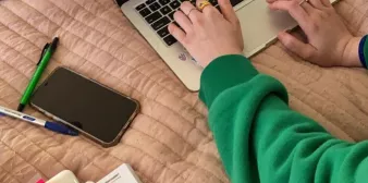 Hands over a laptop next to a phone and textbook