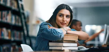 Student leaning on textbooks in library
